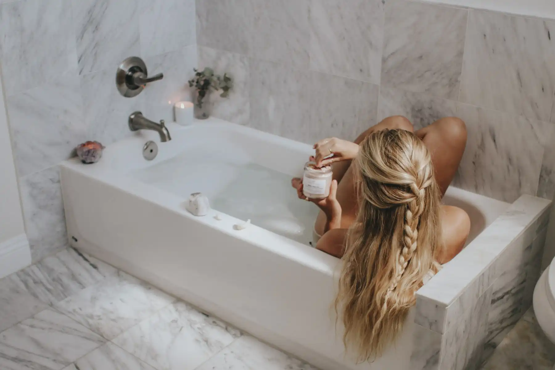 Girl holding a pinch of Himalayan salt above a bathtub filled with steaming water, ready to add it for a relaxing bath