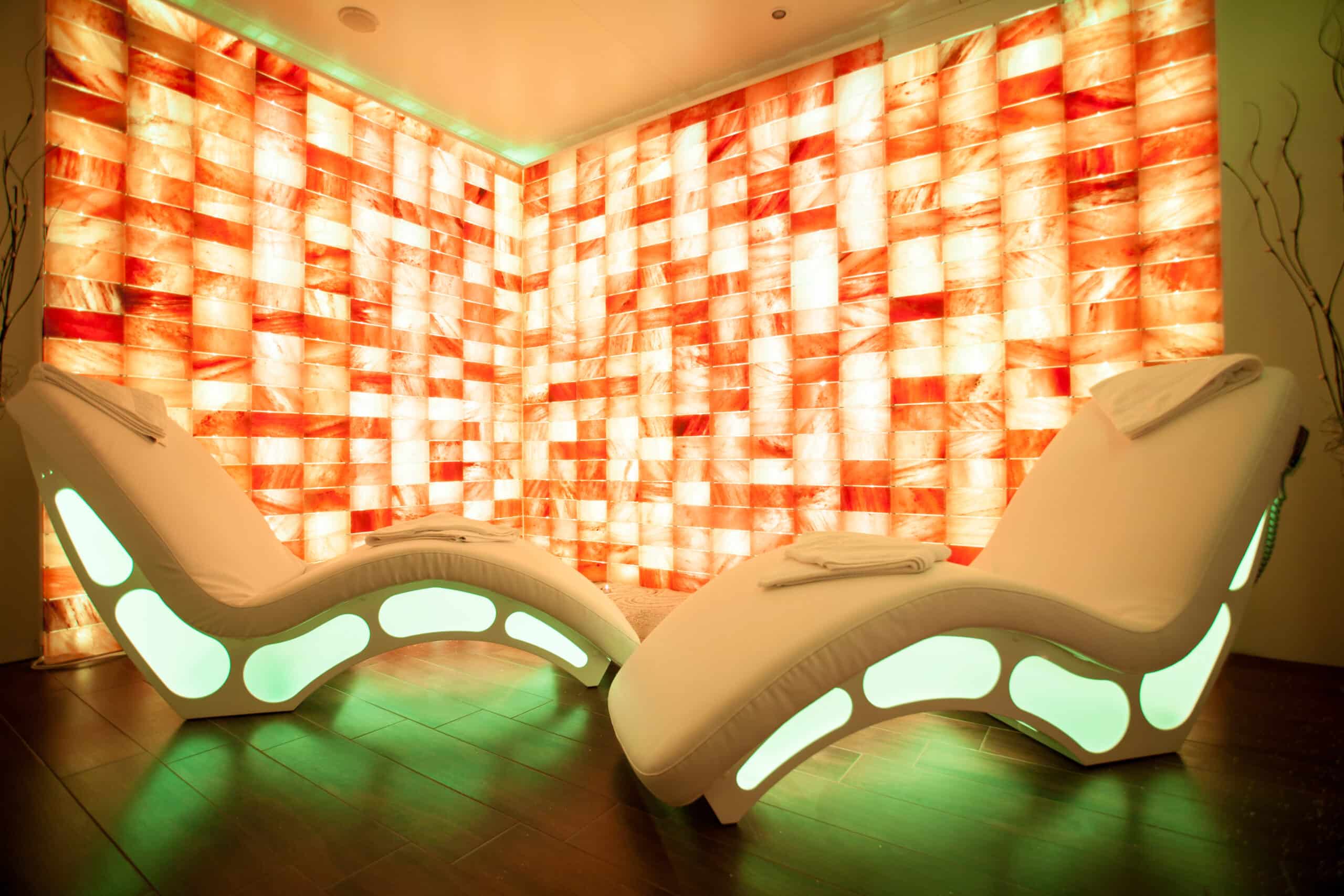 Image of a serene salt room interior featuring two plush armchairs positioned in front of a wall of illuminated Himalayan salt bricks, creating a warm and calming atmosphere.