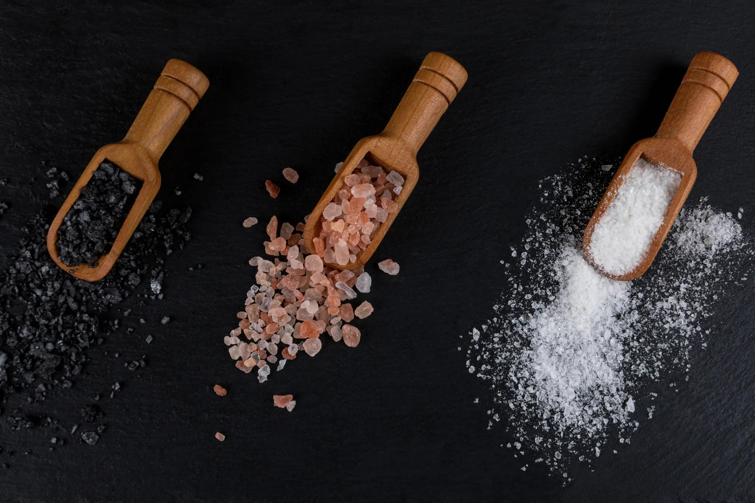 Close-up photo of three wooden spoons filled with different colored Himalayan salt: pink, white, and black.
