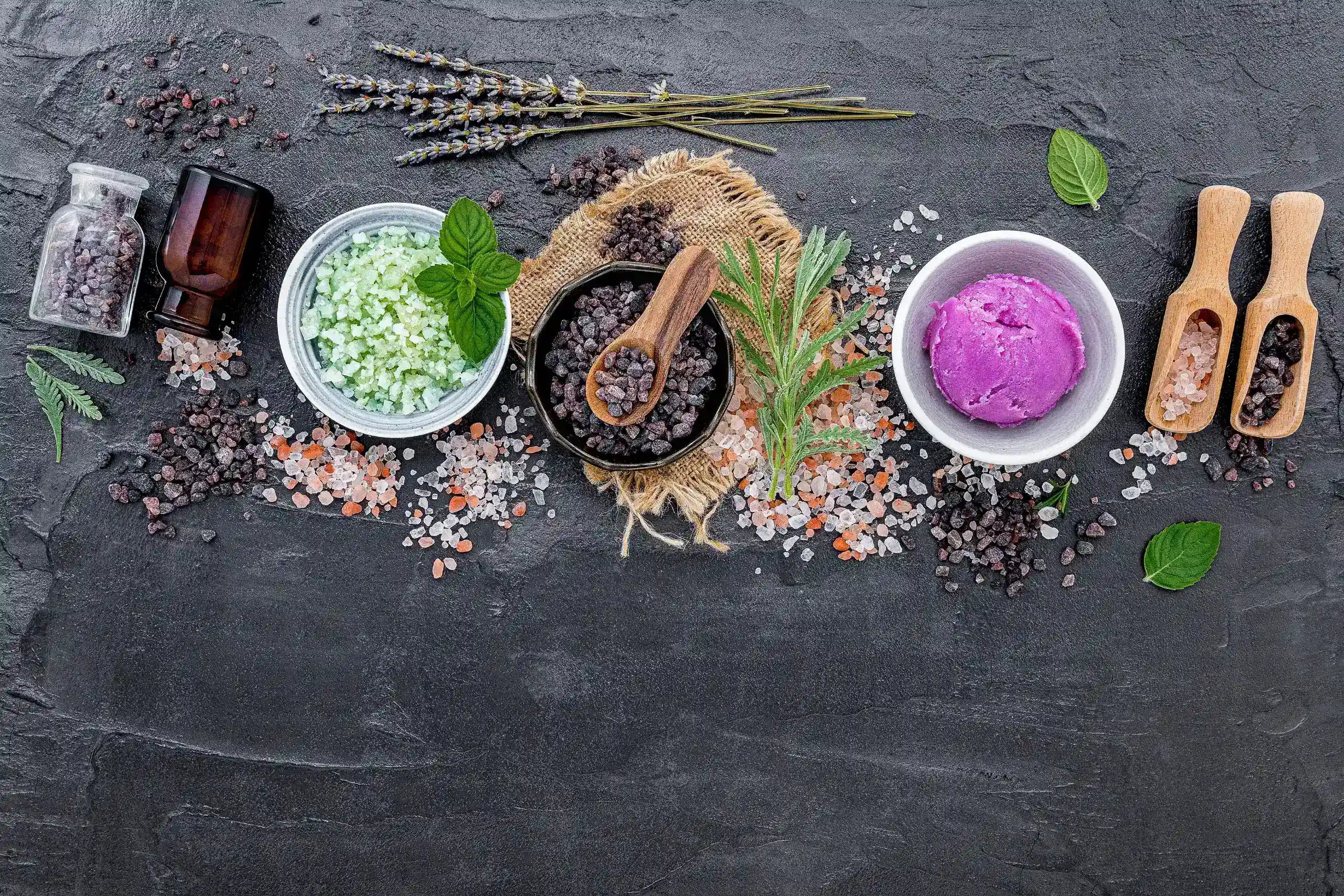 Assorted Himalayan bath salt varieties including mint, lavender, natural, and black salt in scoops and bottles